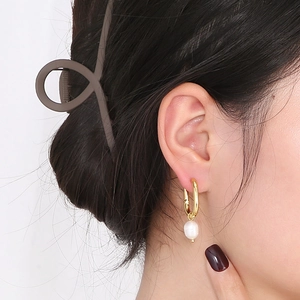 Detail of golden pearl hoop earring and matte coffee hair claw clip on model