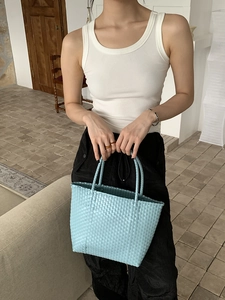 Close-up of light blue straw woven tote bag held by a model in a summer setting