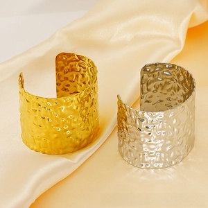 Detail shot of hammered wide cuff bracelets in gold and silver on silk fabric
