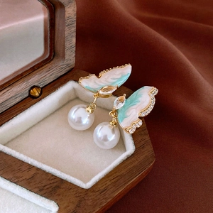 Macro detail of elegant butterfly pearl drop earring on luxury brown silk and wooden box