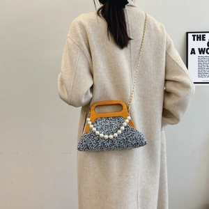 Gray tweed handbag with wood handle and pearl chain shown on beige coat model