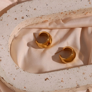 Détail de boucles d'oreilles créoles facettées en acier doré 18 carats sur soie rose