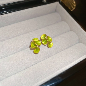 Detailed close-up of vintage gold metal earrings with green enamel on a gray velvet tray