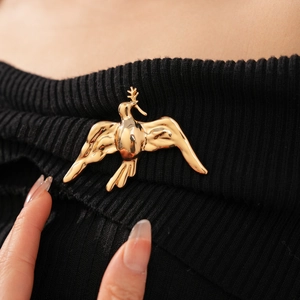 Close-up of a golden flying bird brooch with olive branch on black knit sweater