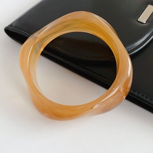 Detail of amber resin bangle with thick wavy design on black leather background
