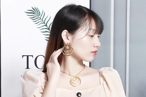 Detail of a model wearing golden geometric multi-layered hoop earrings and a pendant necklace