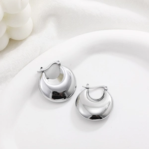 Detailed view of silver polished C-shape hoop earrings on a ceramic dish with fabric background