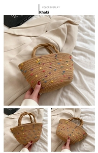 Detail of khaki straw bucket bag featuring colorful pom-pom accents and woven handles