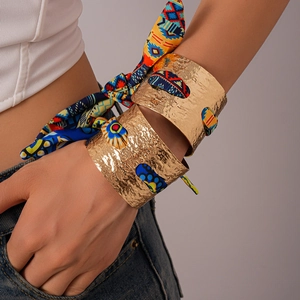 Dettaglio di bracciali dorati testurizzati intrecciati con una sciarpa di seta colorata