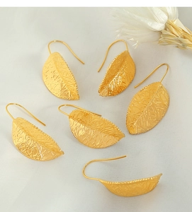 Artistic golden leaf earrings with hollow vein texture on white textured fabric backdrop