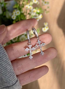 Detailed close-up of silver cross hoop earrings with sparkling cubic zirconia in sunlight