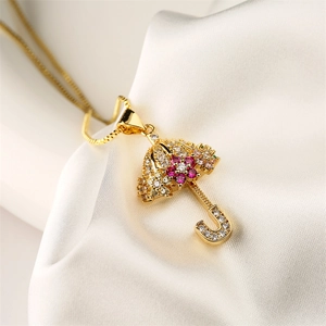 Detailed view of gold umbrella pendant with red and clear cubic zirconia on white silk