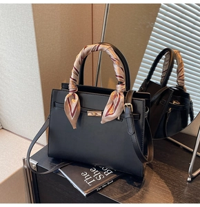 Close-up of a black structured handbag with gold hardware and silk scarf wrap on handle