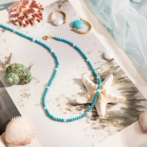 Detailed view of turquoise bead necklace and gold rings with starfish beach decor