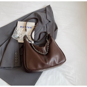 Detail of dark brown leather underarm bag with silver chain on grey blazer background