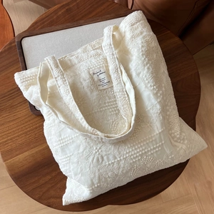 Close-up of cream lace embroidery on tote bag with vintage floral texture on wooden table