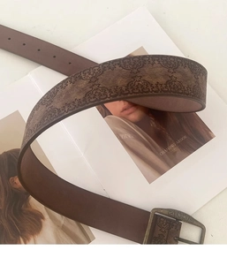 Close-up of brown vintage embossed leather belt with an antique bronze buckle on a magazine