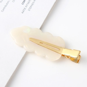 Detailed close-up of a leaf-shaped acetate hair clip with a cream white finish and gold base