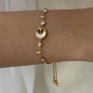 Detail of adjustable gold bracelet featuring shell moon, star charms and zircon stones