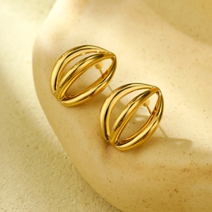 Macro shot of 18K gold hollow oval earrings with layered irregular lines on sandy texture