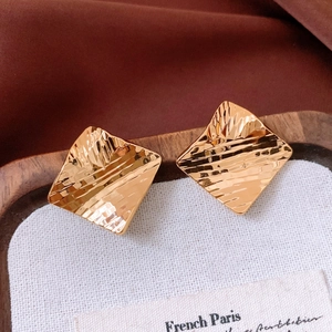 Detailed close-up of 18k gold plated square stud earrings with hammer texture on white canvas