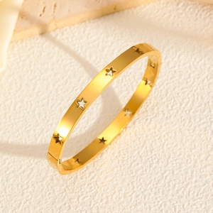 Detailed view of the gold hollow star bangle with a hinge clasp on textured background