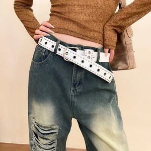 Détail d'une ceinture punk blanche en cuir à œillets argentés sur un jean bleu denim