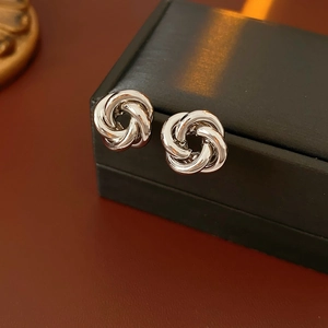 Close-up of silver intertwined metal stud earrings with polished finish on black box