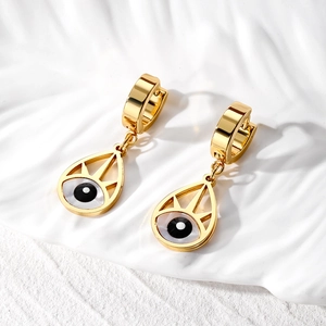 Macro detail of gold teardrop evil eye earrings on a white textured ceramic tray