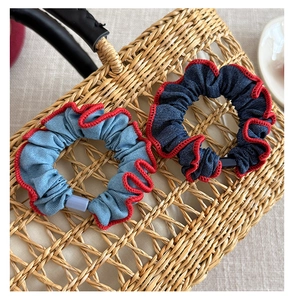 Detail of denim blue scrunchies with red wavy edge stitching on a natural straw bag