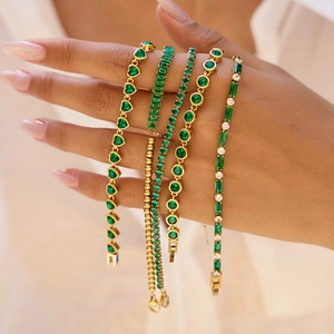 Détail de cinq bracelets dorés superposés avec pierres vertes en forme de cœur et carrées