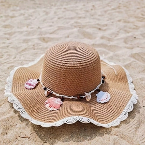 Detail of wide brim straw sun hat with shell and wood bead charms on the beach