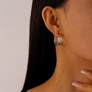 Macro shot of silver C-shape metal earrings with irregular wrinkled texture on model