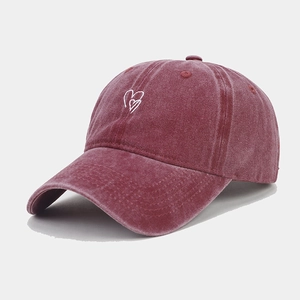 Detail view of washed cotton baseball cap with white heart embroidery on burgundy fabric