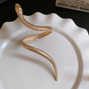 Detail of golden snake bracelet with scale texture displayed on a white ceramic dish