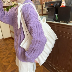 Detail einer großen weißen Falten-Tasche mit Schleifenbändern und violettem Strickpullover