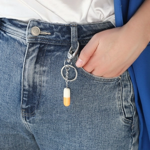 Minimalist resin capsule keychain in orange and white attached to denim jeans belt loop