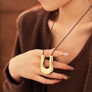Détail d'un grand pendentif doré en forme de U sur un cordon de collier noir minimaliste