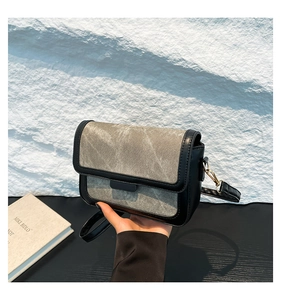 Detail of grey washed texture crossbody bag with black leather trim and gold buckle