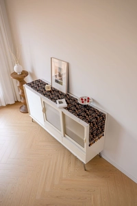 Detail of a black floral jacquard table runner with fringe on a white sideboard cabinet
