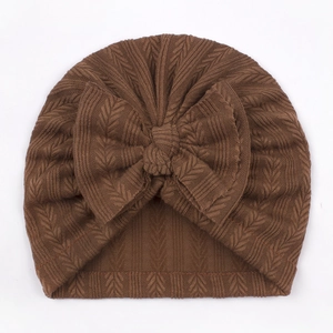 Close-up of dark brown knitted baby turban hat with a large bow detail and V-pattern