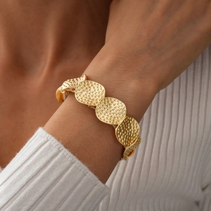 Detailaufnahme eines goldenen Armbands mit gehämmerten Metallscheiben am Handgelenk