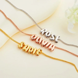 Custom 18K bubble letter name necklaces in gold, rose gold and silver on soft fabric