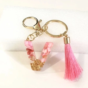 Detail of letter V resin keychain with pink flower petals, gold flakes and silk tassel