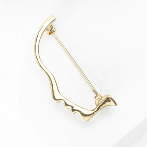 Macro shot of gold creative face brooch pin with wavy curved design on white background