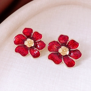 Macro detail of red enamel flower earrings with golden rose center on textured background