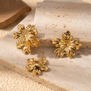 Double-layered gold flower earrings in stainless steel displayed on a natural stone slab