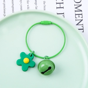 Close-up of green flower keychain with metal bell on a green ceramic plate