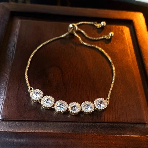 Detail of adjustable gold-plated bracelet with sparkling square zircons on wood