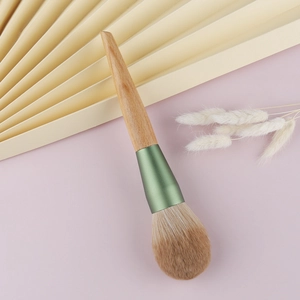 Large fluffy powder brush with natural wood handle and matte green ferrule on soft background